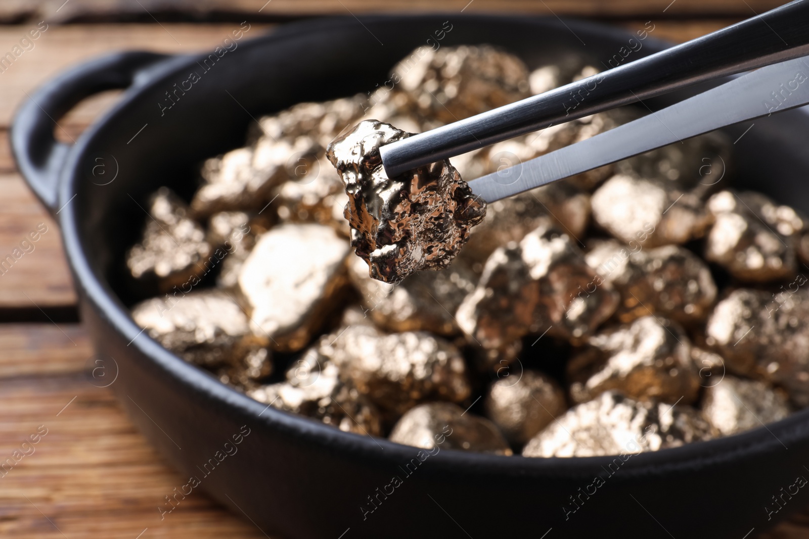 Photo of Tweezers with gold nugget on blurred background, closeup