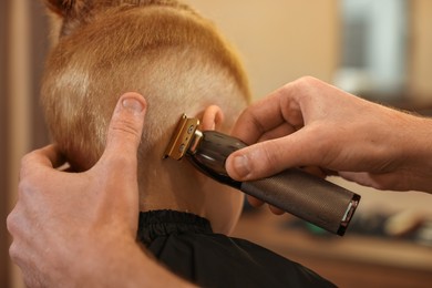 Photo of Professional hairdresser cutting boy's hair in beauty salon, closeup