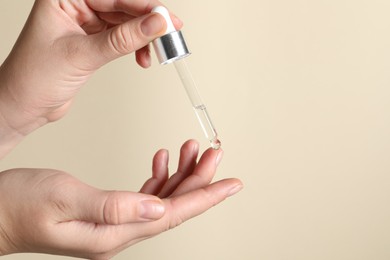 Photo of Woman applying cosmetic serum onto finger on beige background, closeup. Space for text
