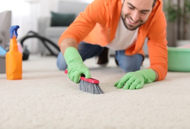 Photo of Young man cleaning carpet at home