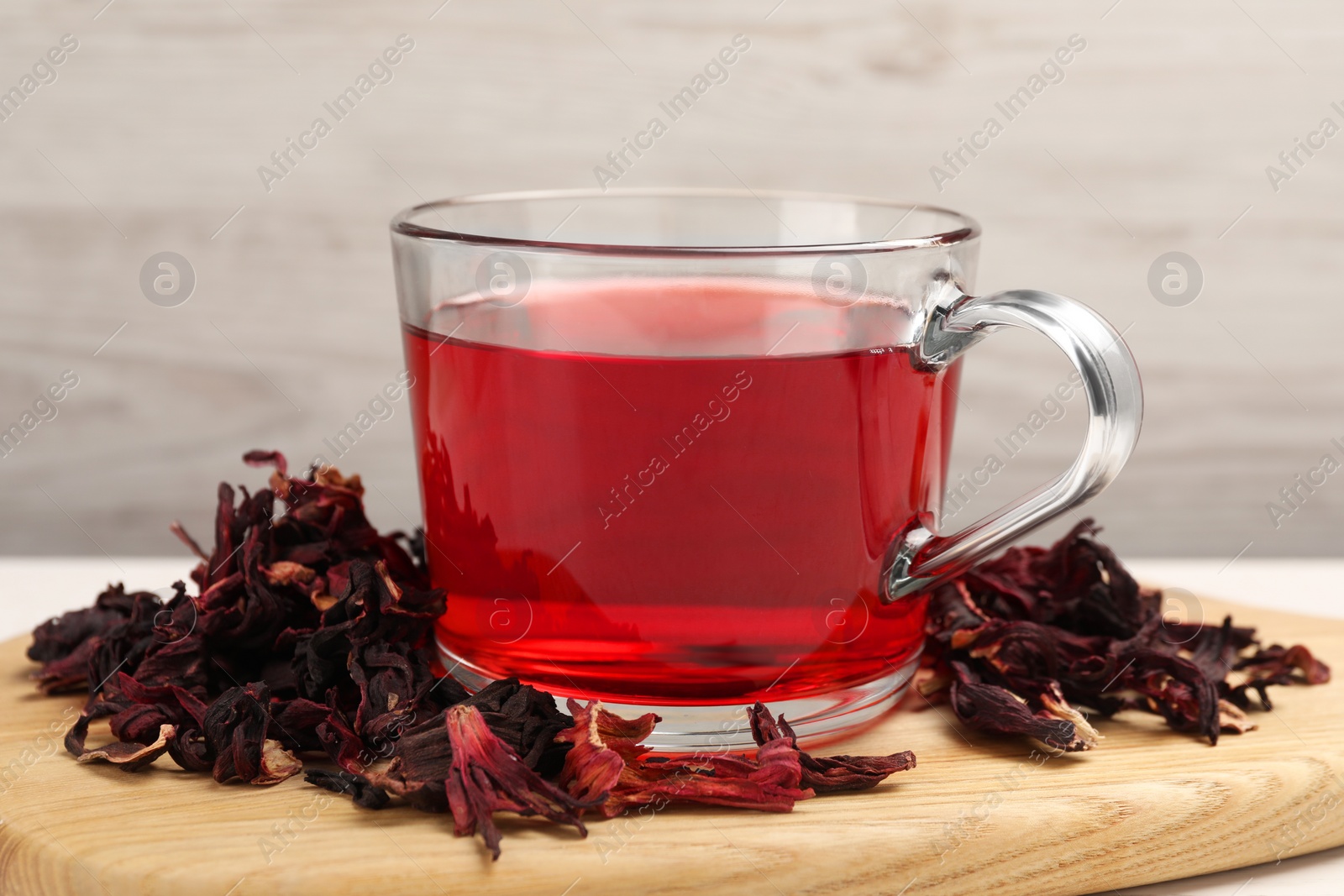 Photo of Cup of fresh hibiscus tea and dry flower leaves on wooden board