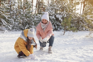 Photo of Mother and daughter rolling snowballs in winter forest