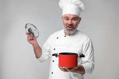 Surprised chef in uniform with cooking pot on grey background