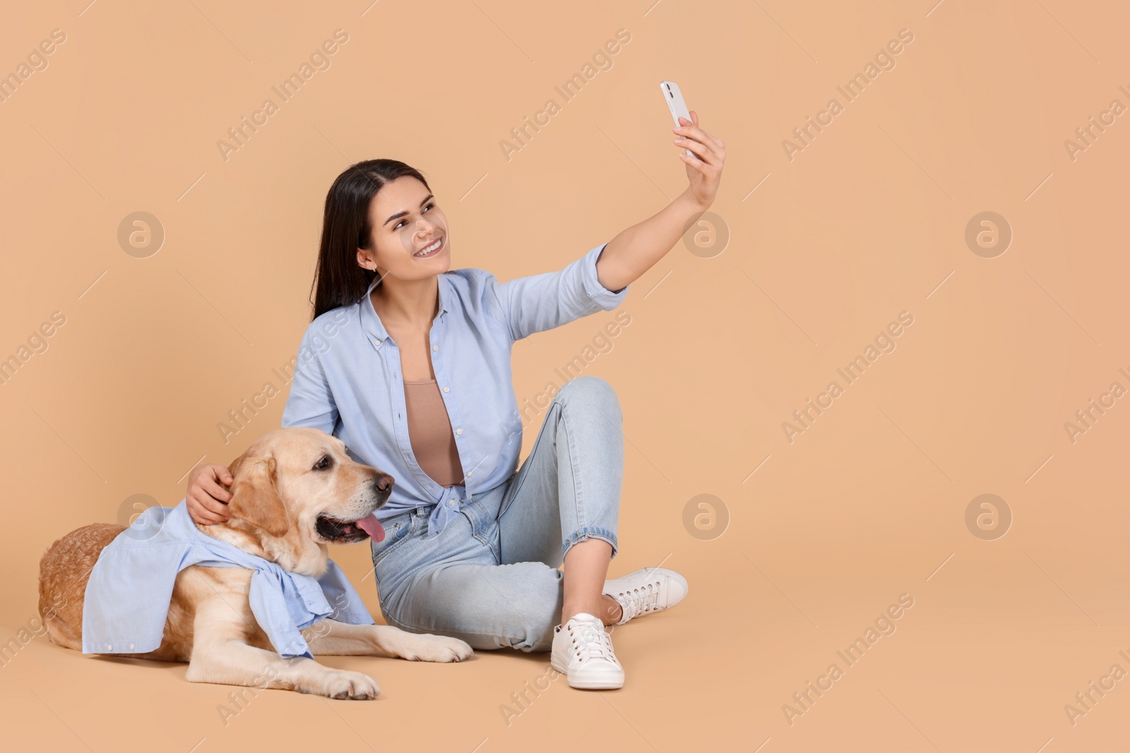 Photo of Happy woman taking selfie with cute Labrador Retriever on beige background. Space for text