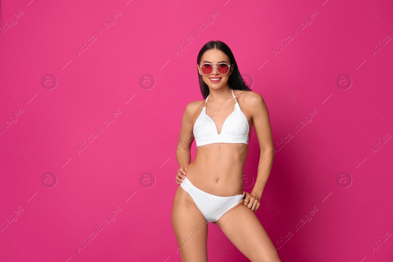 Photo of Beautiful young woman in white bikini with sunglasses on pink background. Space for text