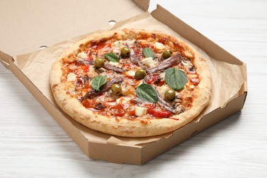 Photo of Tasty pizza with anchovies, basil and olives on white wooden table