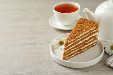 Photo of Slice of delicious layered honey cake served with tea on wooden table. Space for text
