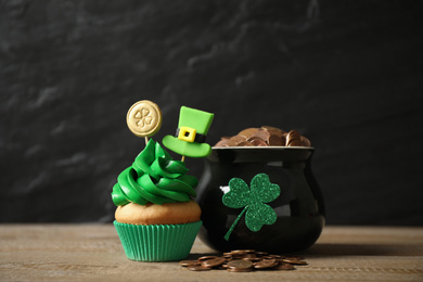 Photo of Decorated cupcake and pot with gold coins on wooden table. St. Patrick's Day celebration