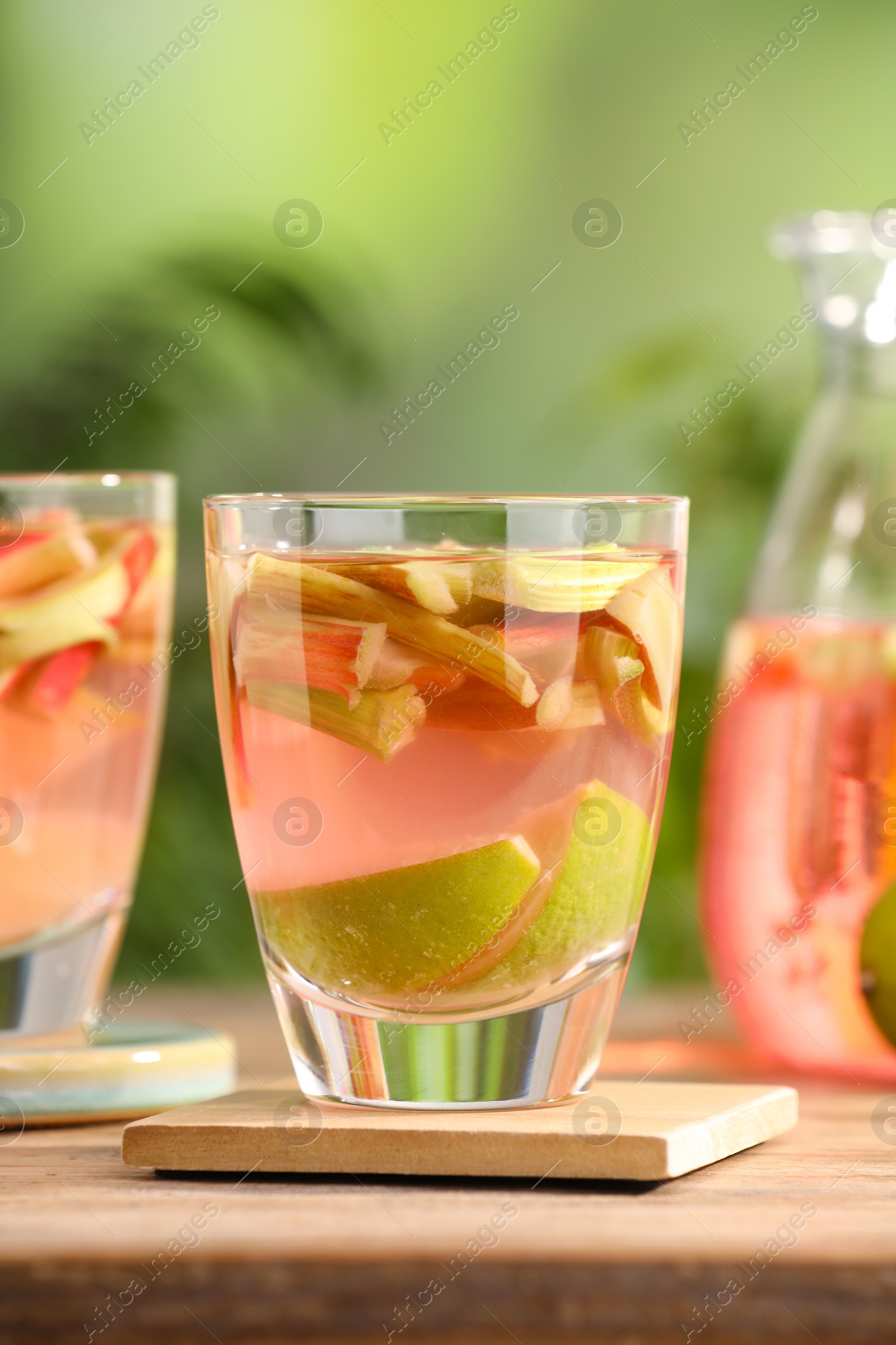 Photo of Glass of tasty rhubarb cocktail with lime fruits on wooden table outdoors, closeup