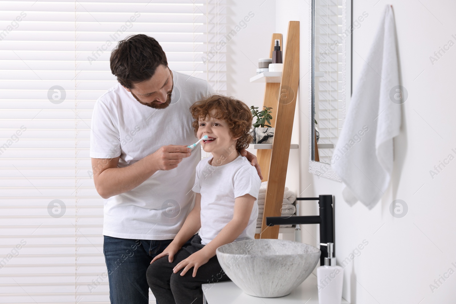 Photo of Father helping his son to brush teeth in bathroom