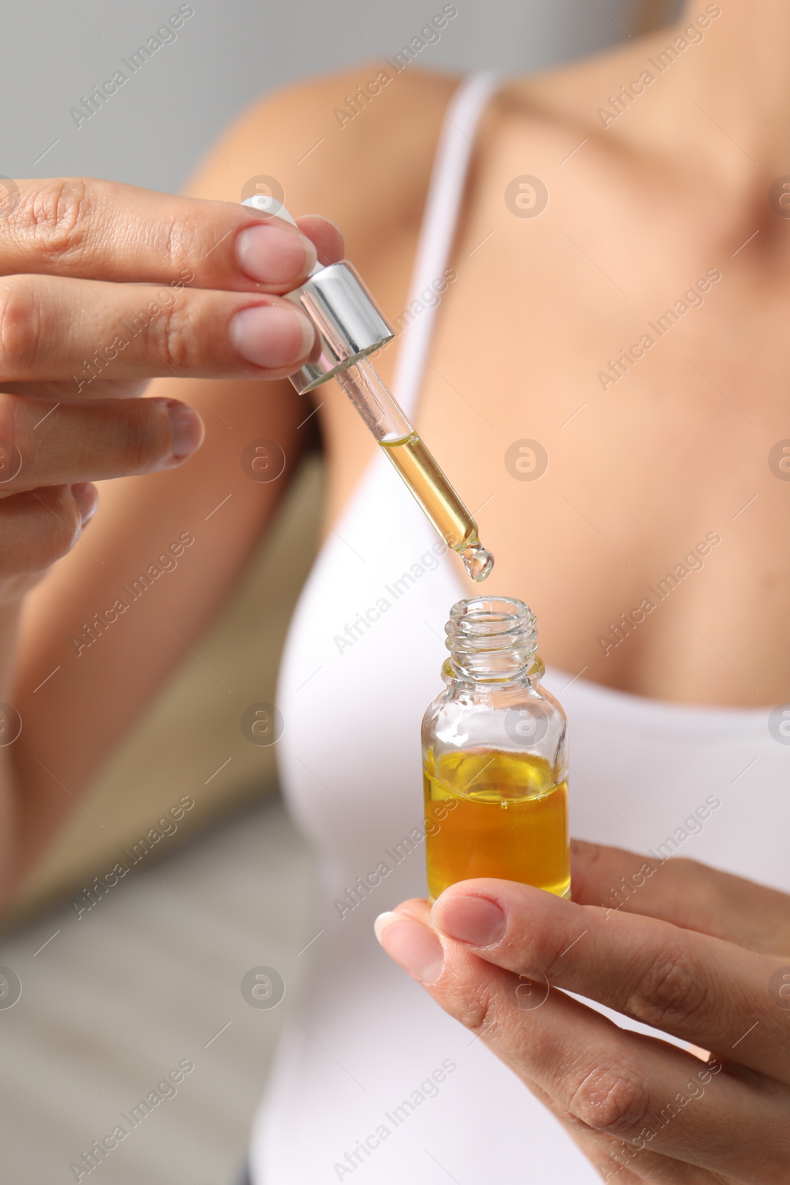 Photo of Woman with bottle of cosmetic serum on blurred background, closeup