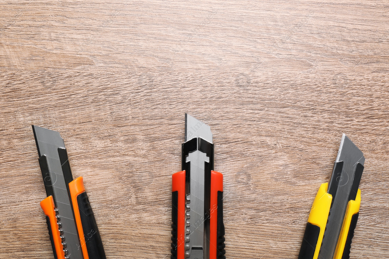 Photo of Three different utility knives on wooden table, flat lay. Space for text