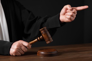 Judge with gavel pointing at wooden table against black background, closeup
