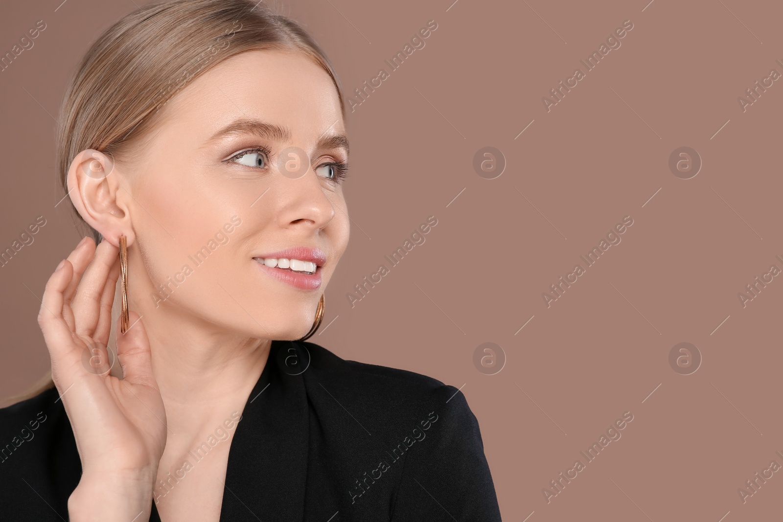 Photo of Beautiful young woman with elegant earrings on light brown background, space for text