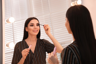 Photo of Beautiful young woman applying makeup near mirror in dressing room