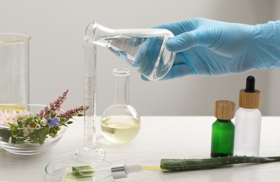 Scientist developing cosmetic oil at white table, closeup