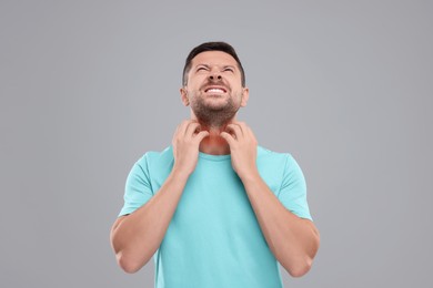 Allergy symptom. Man scratching his neck on light grey background