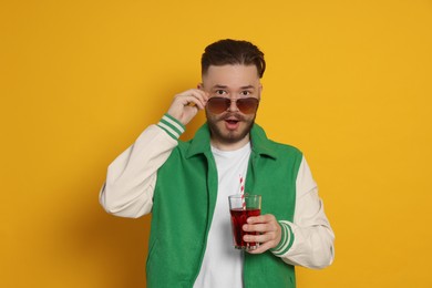 Handsome young man with glass of juice on yellow background