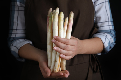 Photo of Woman holding fresh white asparagus on black background, closeup