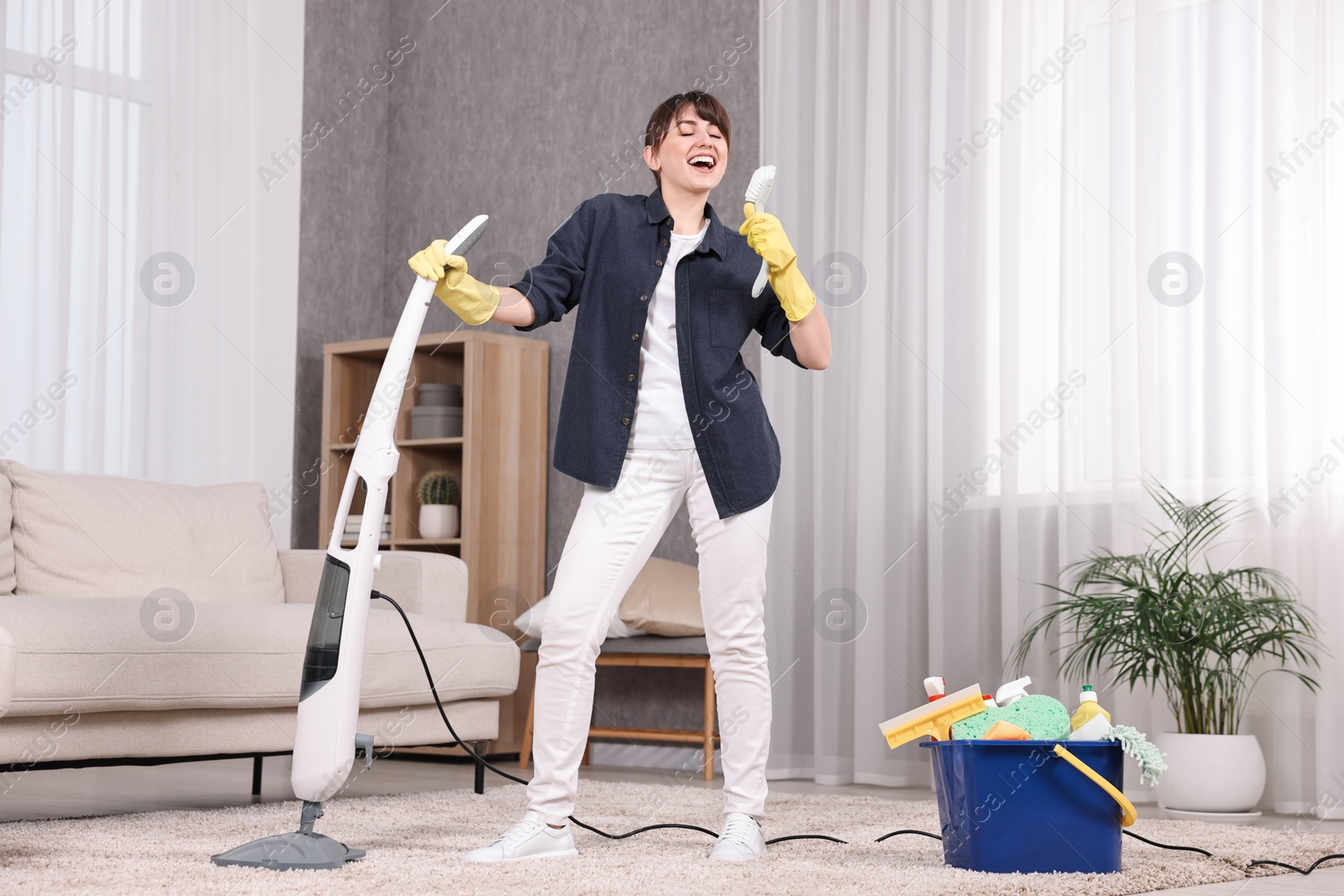 Photo of Happy young housewife having fun while cleaning carpet at home