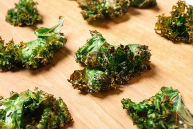 Tasty baked kale chips on wooden table, closeup