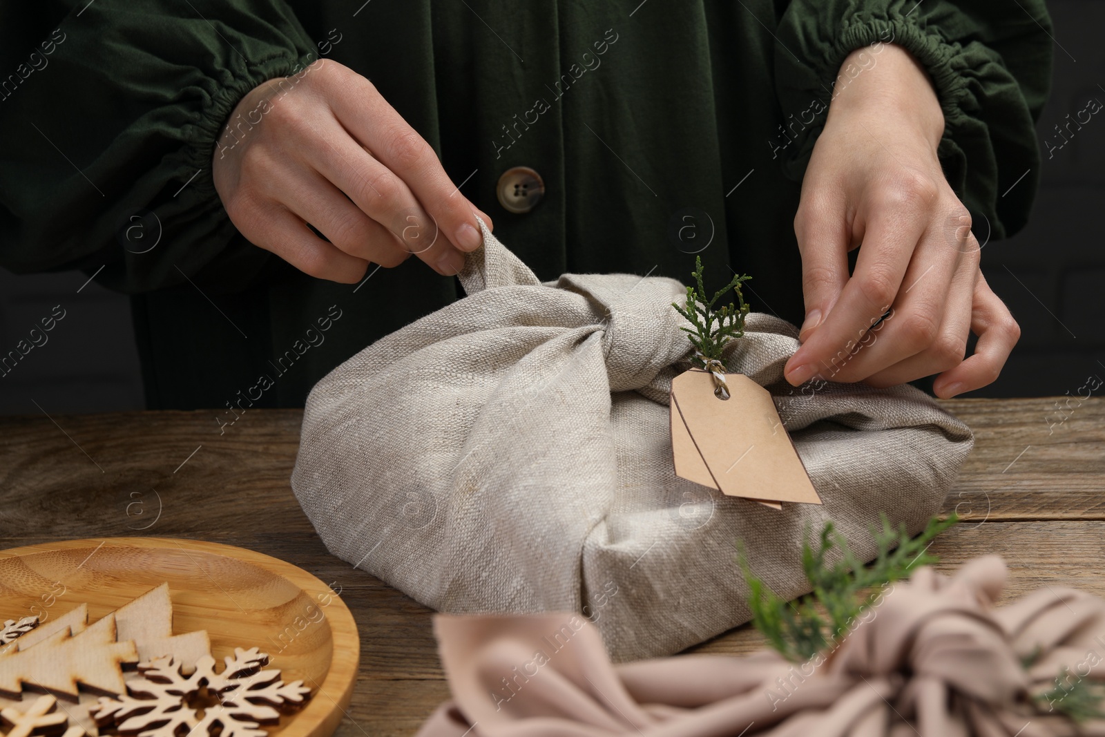 Photo of Furoshiki technique. Woman wrapping gift in fabric at wooden table, closeup