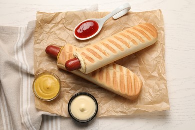 Photo of Tasty french hot dogs and dip sauces on white wooden table, flat lay