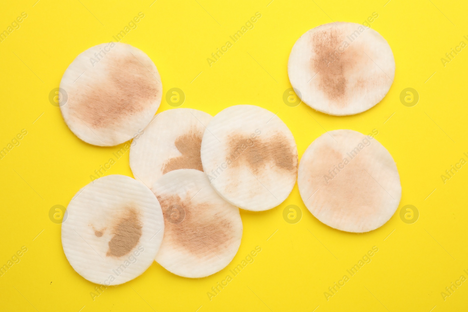 Photo of Dirty cotton pads after removing makeup on yellow background, flat lay