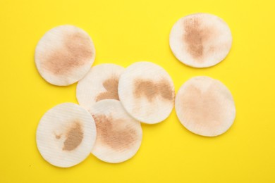 Photo of Dirty cotton pads after removing makeup on yellow background, flat lay