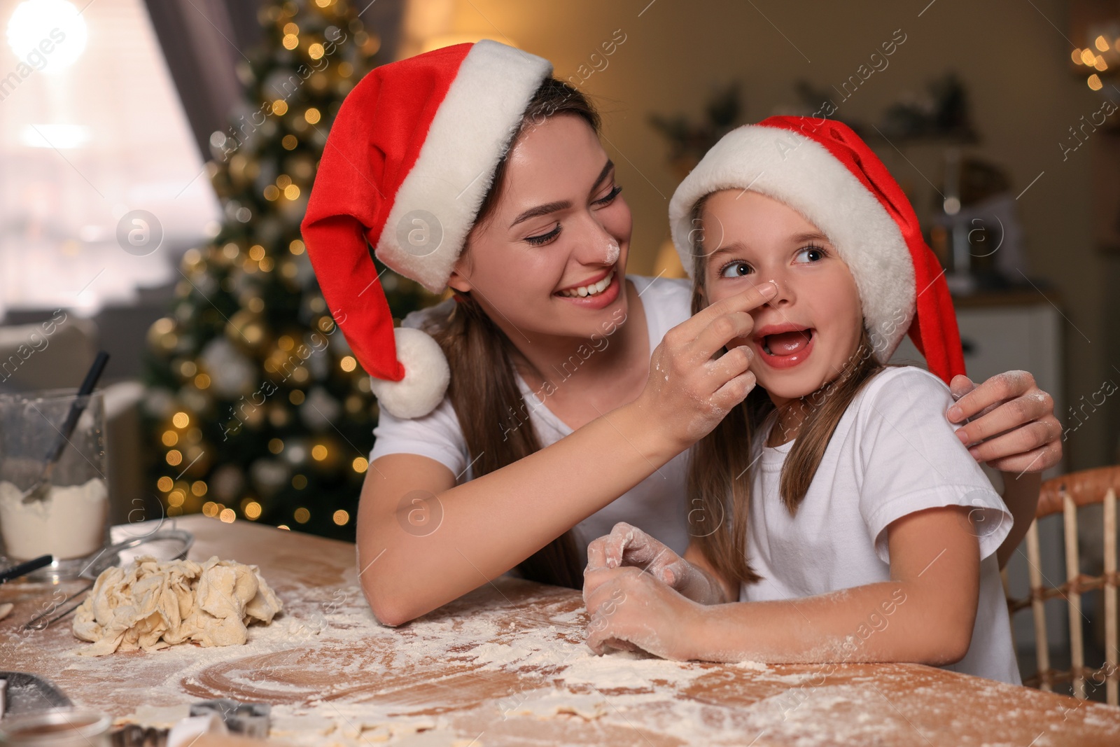 Photo of Mother with her cute little daughter having fun while making dough for Christmas cookies in kitchen