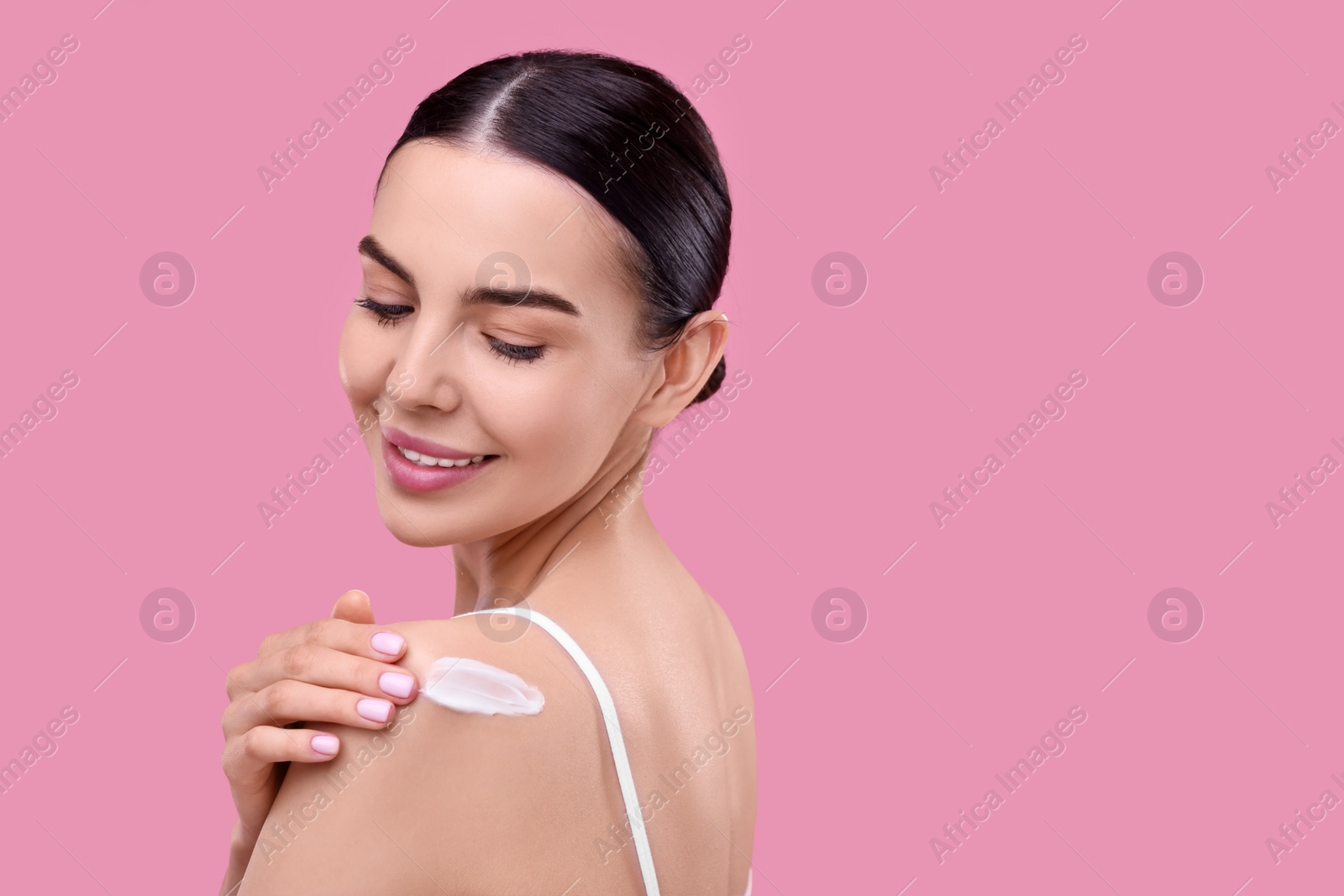 Photo of Beautiful woman with smear of body cream on her shoulder against pink background, space for text