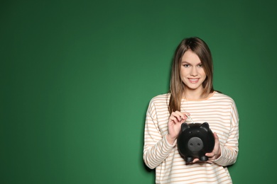 Young woman putting money into piggy bank on color background. Space for text