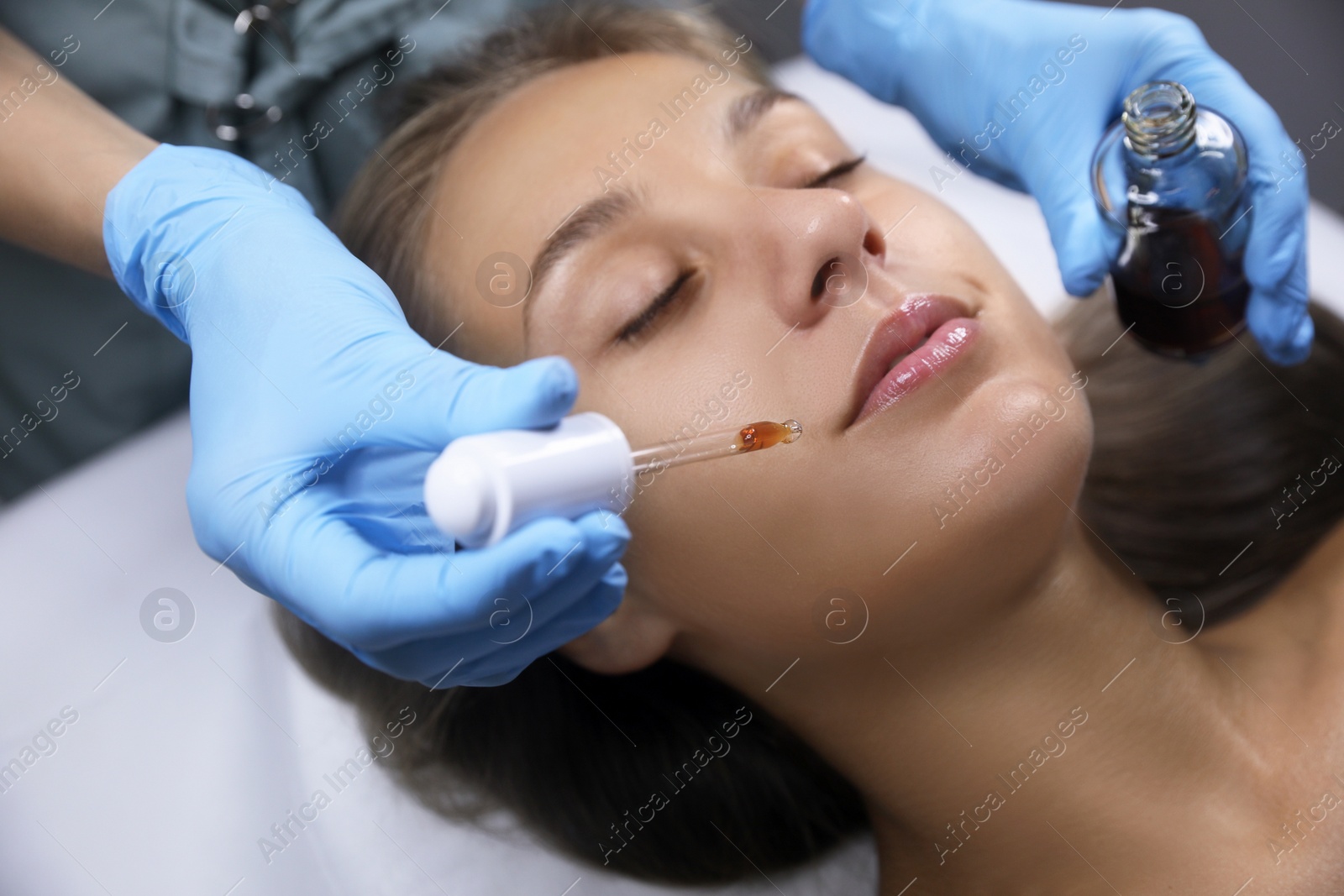 Photo of Cosmetologist applying serum on client's face in salon