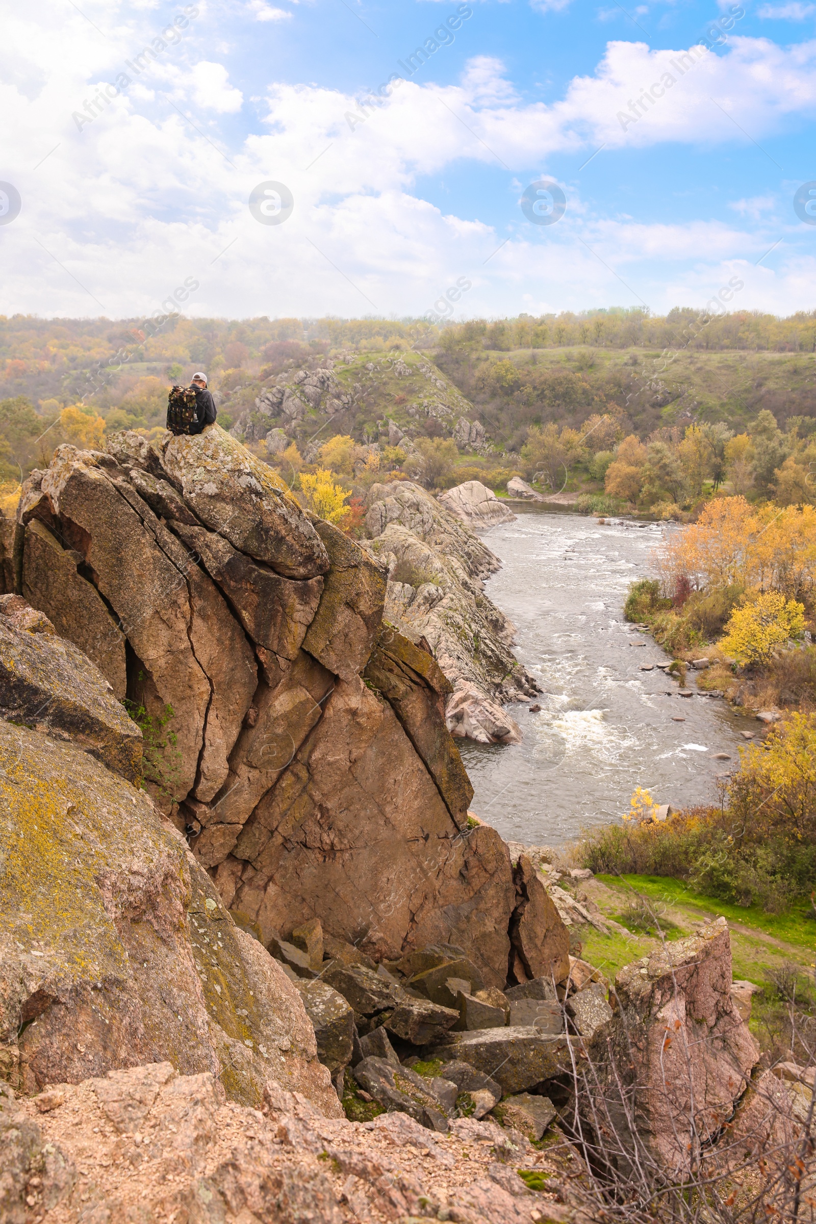 Photo of Hiker with travel backpack sitting on steep cliff near mountain river