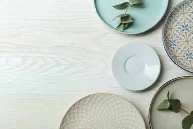 Flat lay composition with beautiful dishware and green leaves on white wooden table, space for text