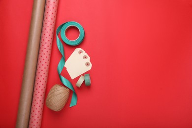 Photo of Rolls of wrapping papers, tags and ribbons on red background, flat lay. Space for text