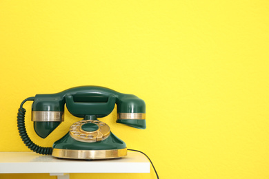 Photo of Green vintage corded phone on white table against yellow background. Space for text