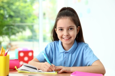 Photo of Little girl doing assignment at desk in classroom. School stationery