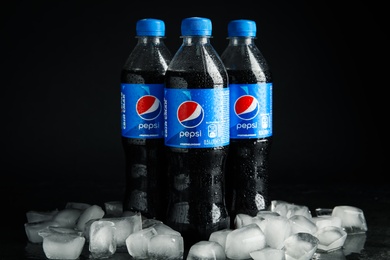 Photo of MYKOLAIV, UKRAINE - FEBRUARY 11, 2021: Plastic bottles of Pepsi with water drops and ice cubes on table against black background