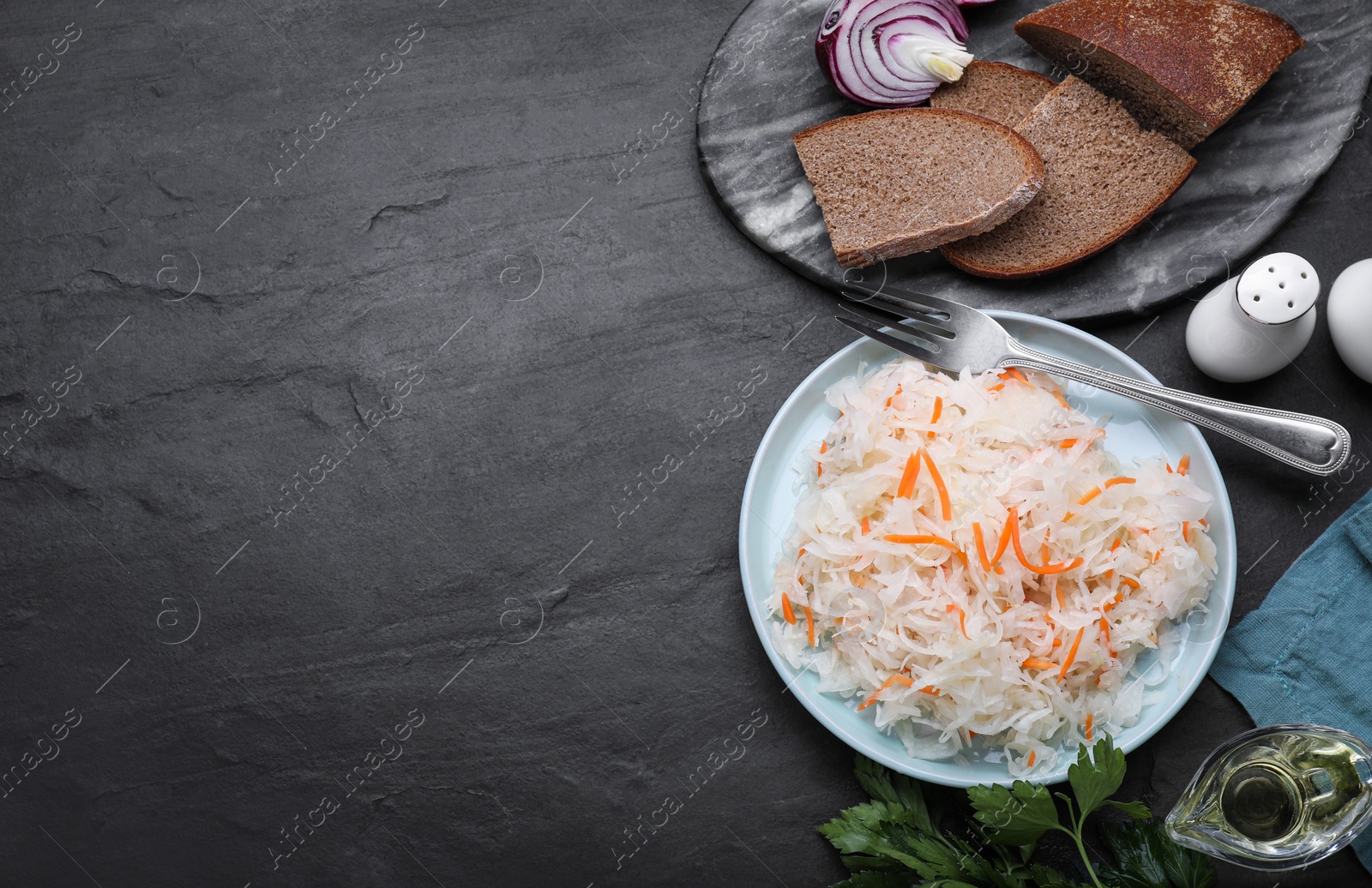Photo of Plate of tasty sauerkraut and ingredients on black table, flat lay. Space for text