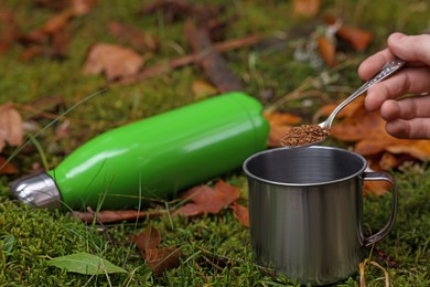 Photo of Woman pouring instant coffee into mug on green grass outdoors, closeup