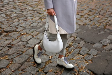Photo of Stylish woman with trendy white baguette bag on city street, closeup