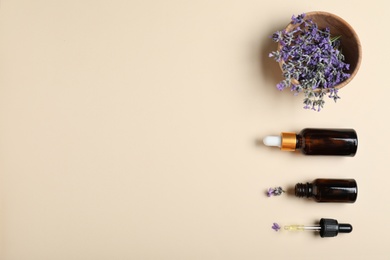 Photo of Bottles of essential oil and lavender flowers in bowl on beige background, flat lay. Space for text
