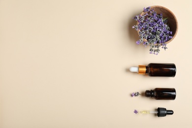 Bottles of essential oil and lavender flowers in bowl on beige background, flat lay. Space for text