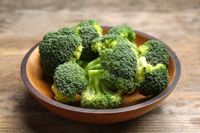 Photo of Wooden bowl of fresh broccoli on table, closeup