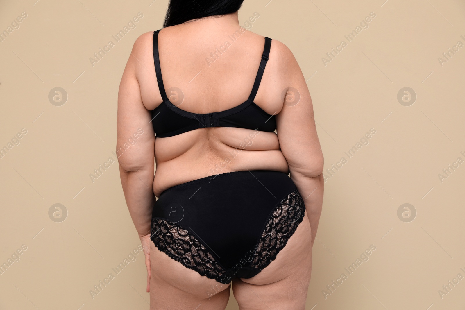 Photo of Back view of overweight woman in black underwear on beige background. Plus-size model