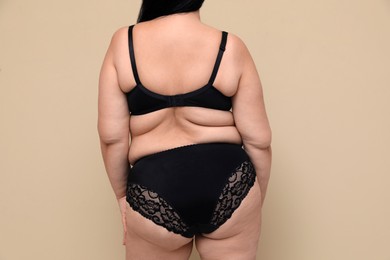 Photo of Back view of overweight woman in black underwear on beige background. Plus-size model