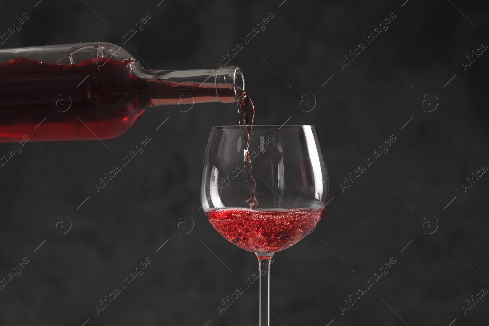 Photo of Pouring red wine from bottle into glass on dark background, closeup