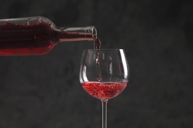 Pouring red wine from bottle into glass on dark background, closeup