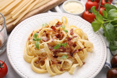 Tasty pasta with bacon and basil on white marble table